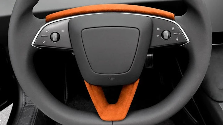 Orange U-shaped Alcantara suede steering wheel panel designed for Tesla Model 3+ with the interior of a car steering wheel in the background.